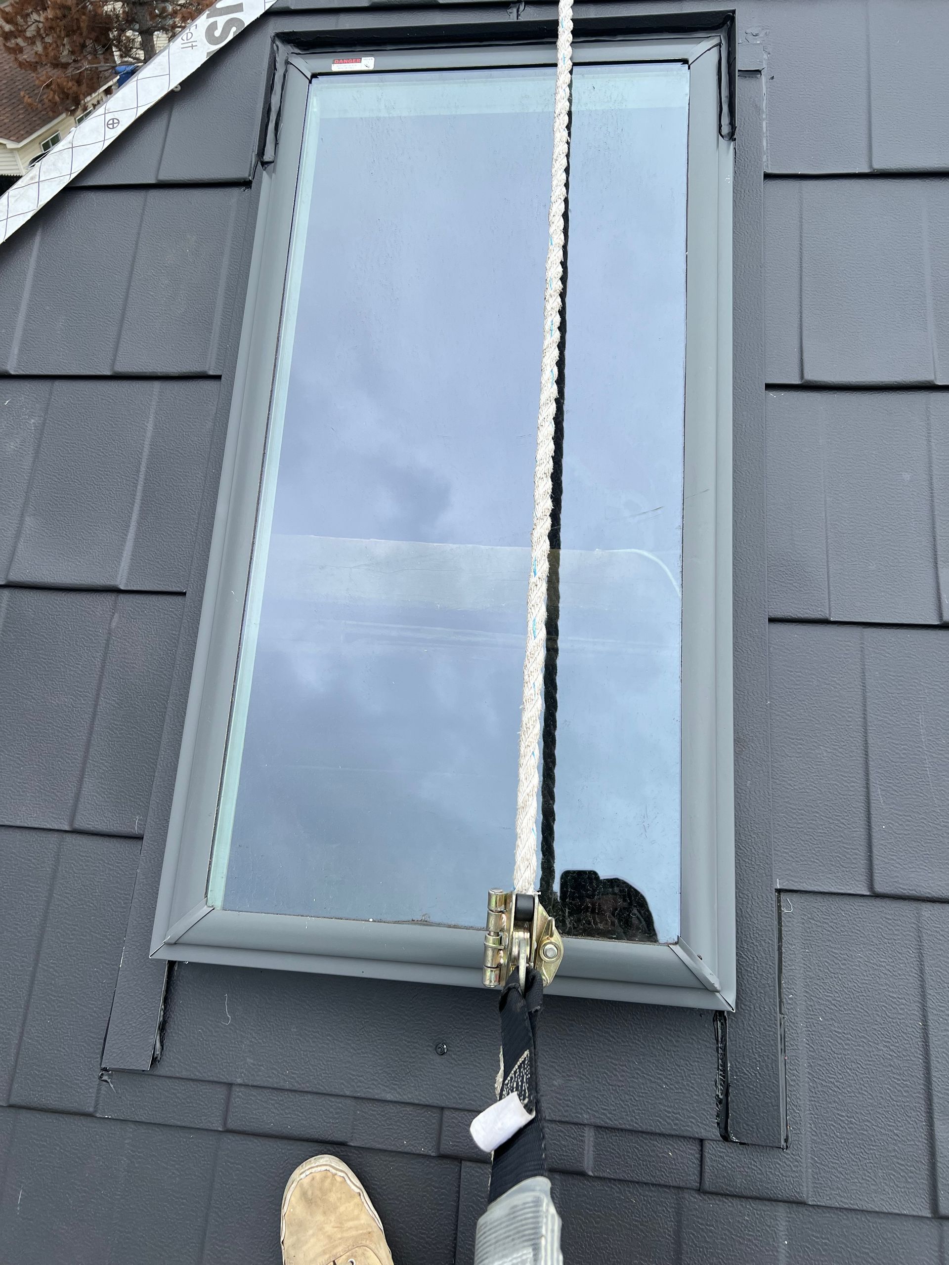 Une personne mesure une lucarne sur un toit avec un ruban à mesurer.