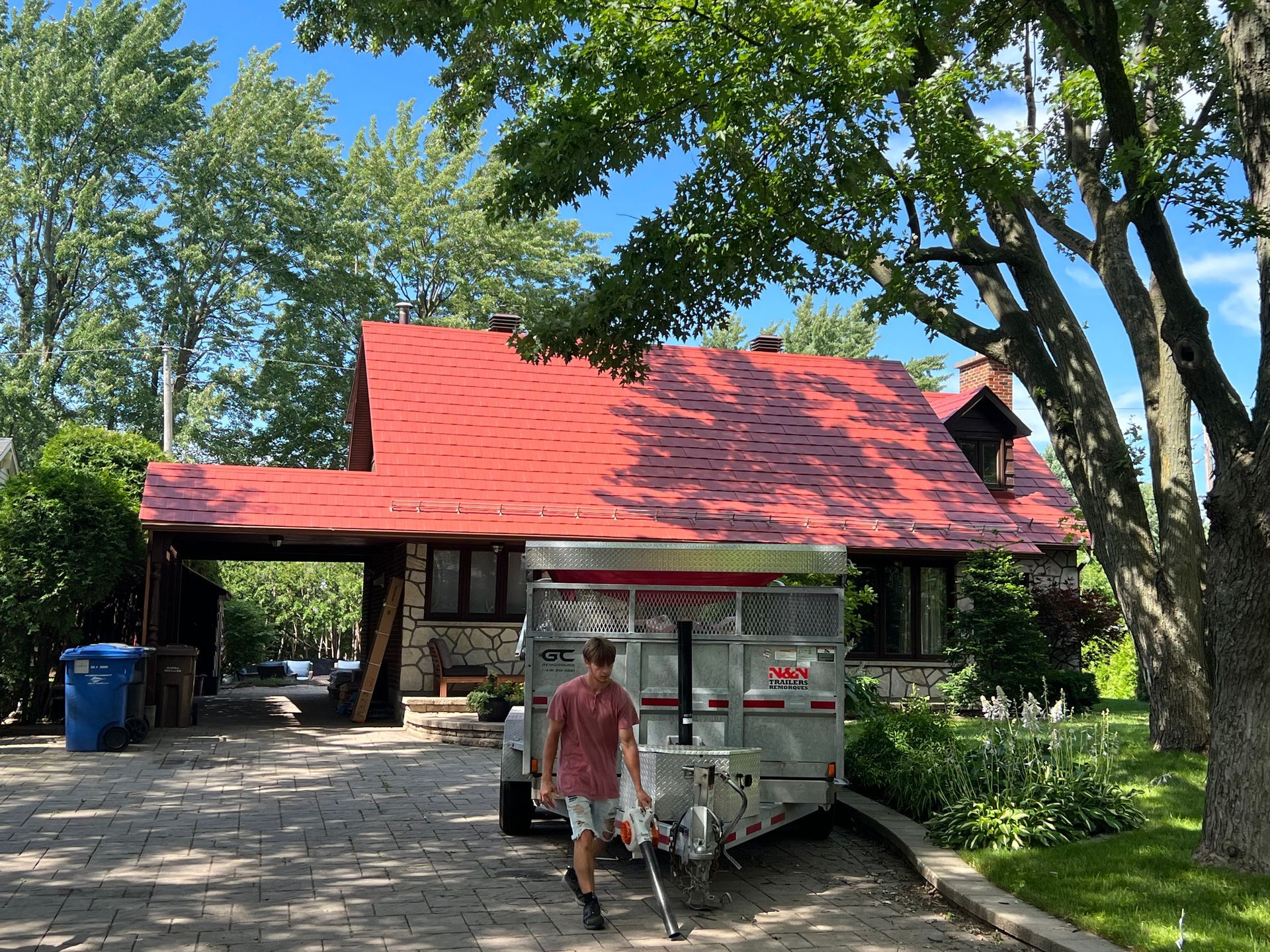 Un homme tire une remorque devant une maison au toit rouge.