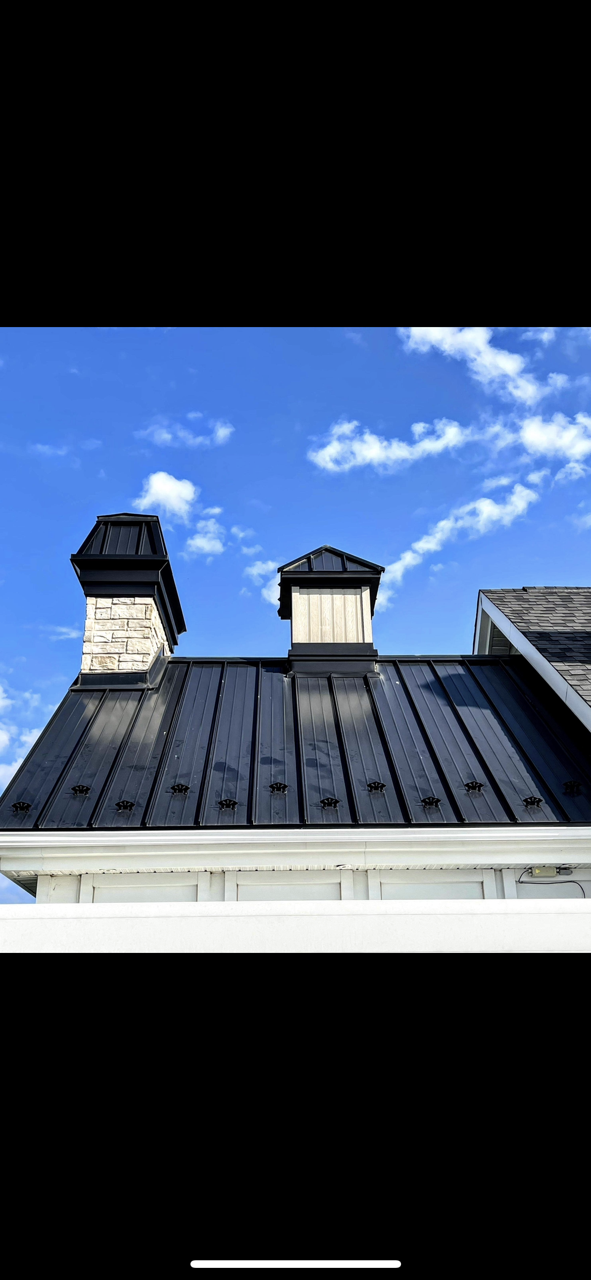 Un toit noir avec des cheminées dessus et un ciel bleu en arrière-plan.