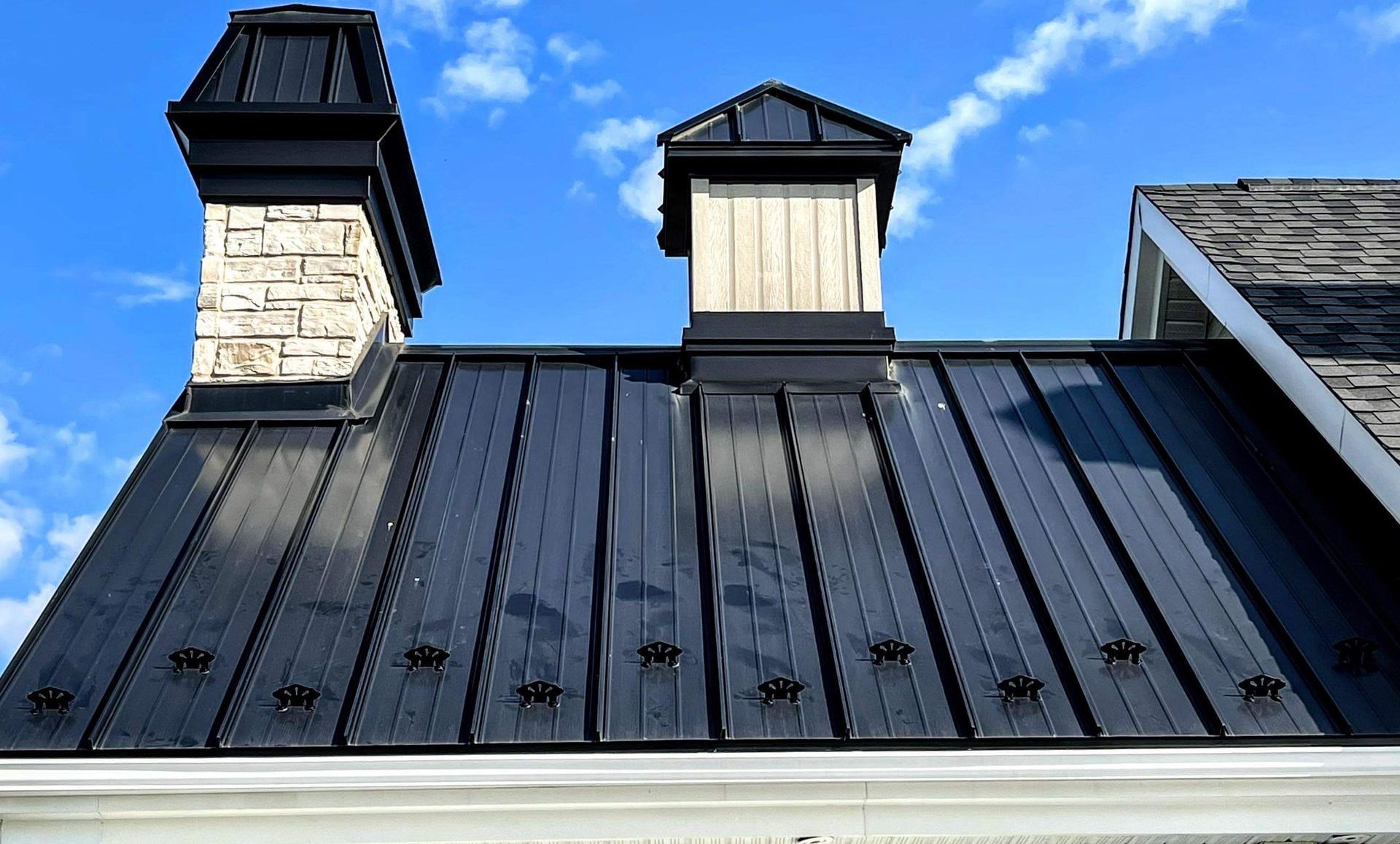 Toit en métal noir avec deux cheminées contre un ciel bleu.