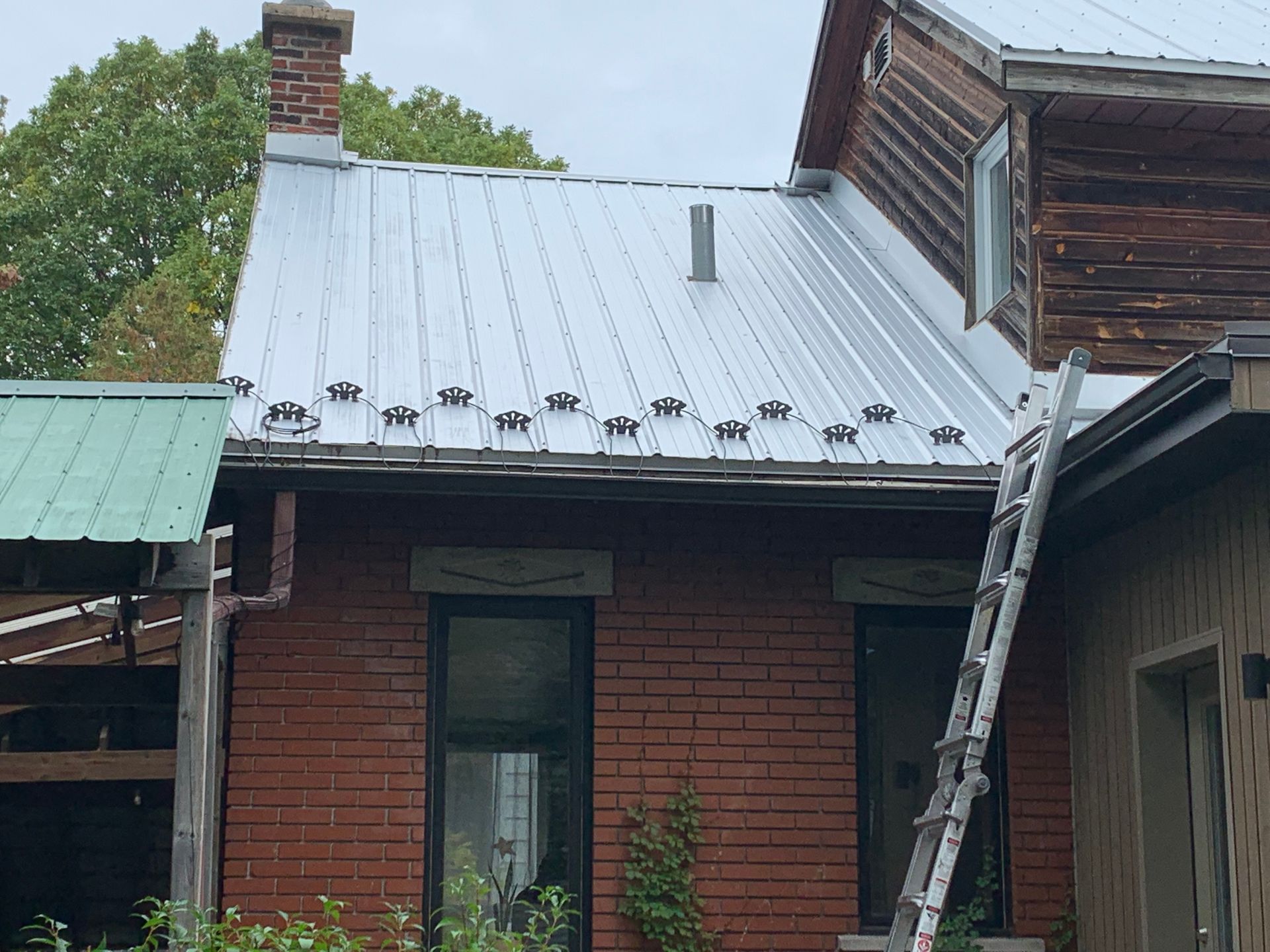 Une échelle est posée sur le côté d'une maison en briques avec un toit en métal.