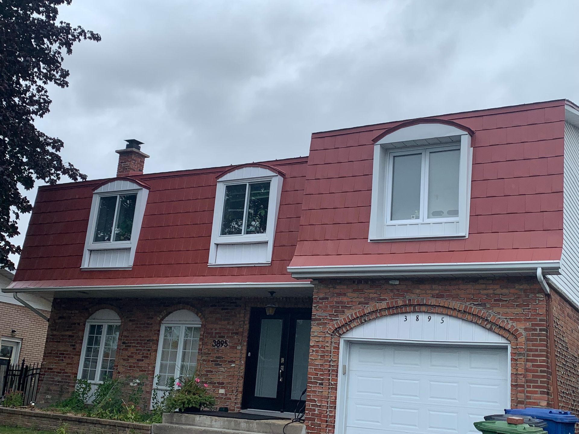 Une maison en brique avec un toit rouge et une porte de garage blanche.