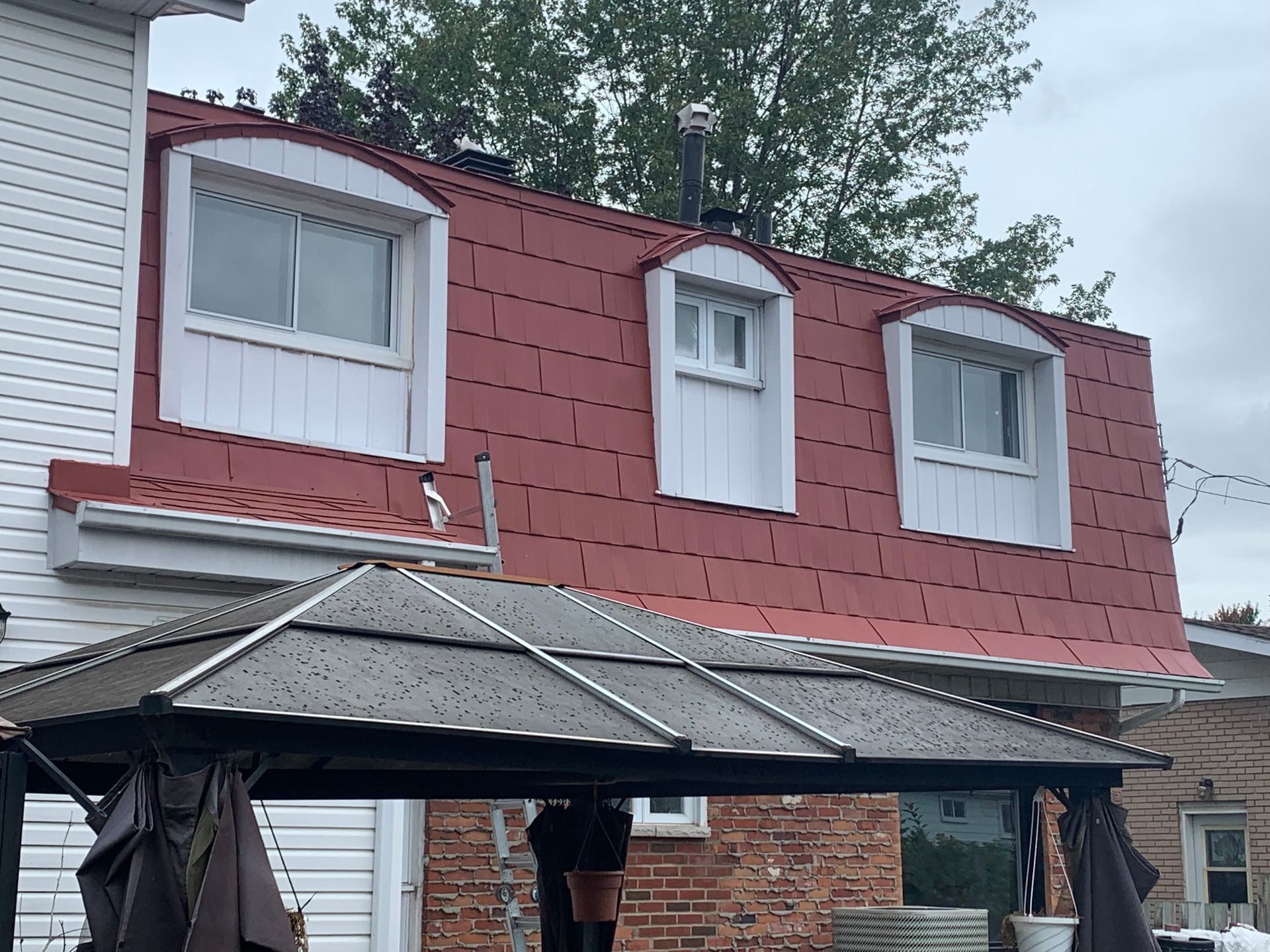 Un homme se tient debout sous un belvédère devant une maison au toit rouge.