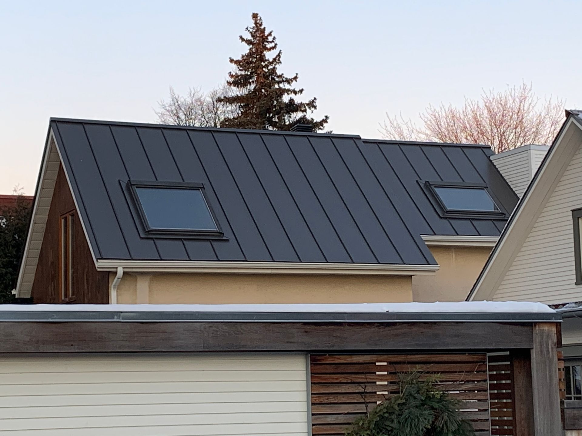 Une maison avec un toit noir et deux puits de lumière