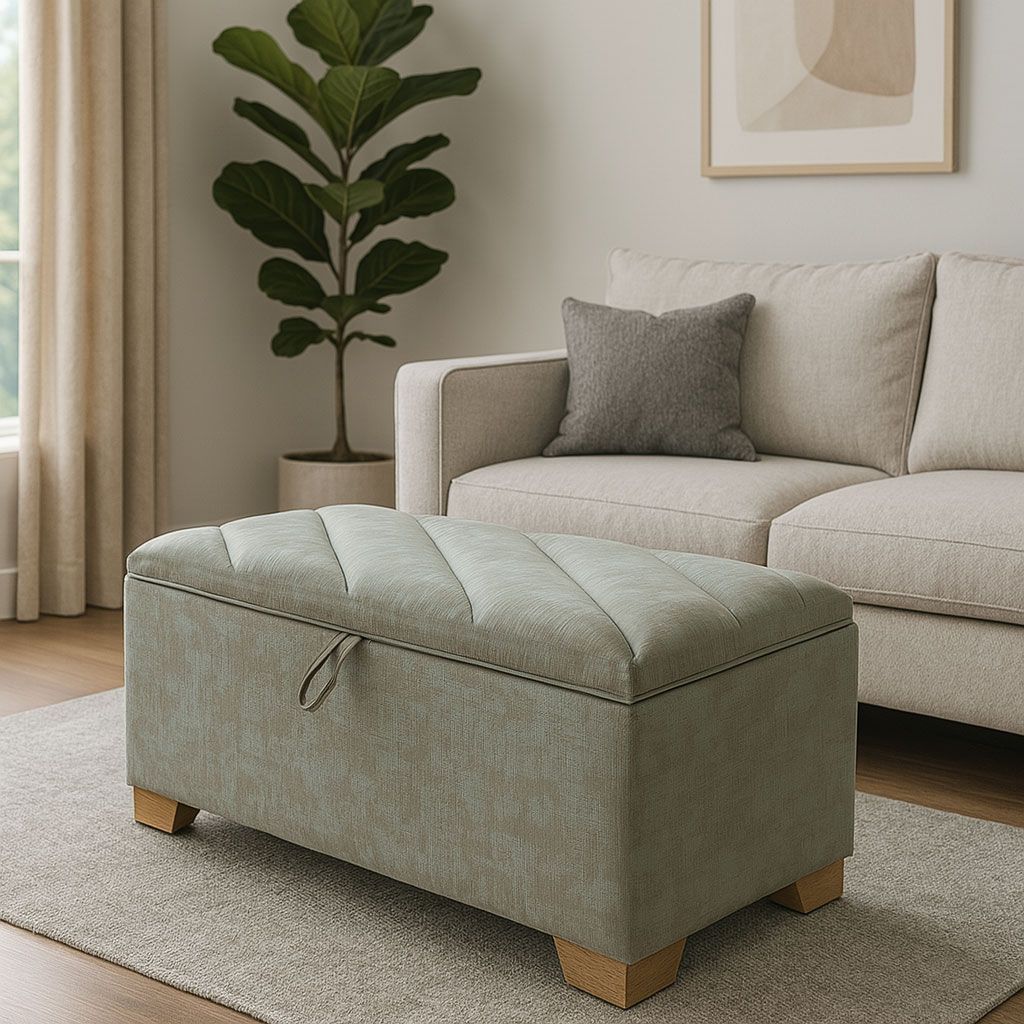 Un puf rectangular tapizado en color verde claro, que sirve de almacenamiento, descansa sobre una alfombra frente a un sofá de color neutro y una planta.