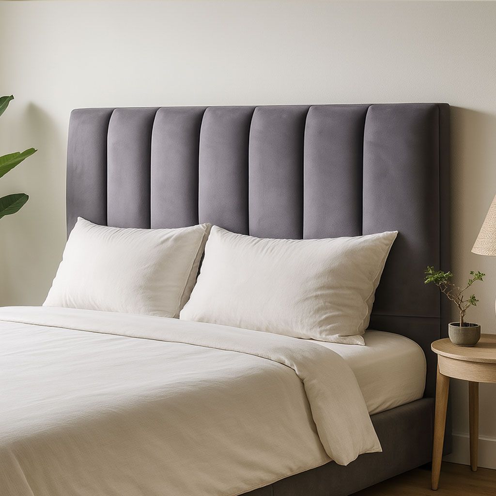 Un cabecero tapizado de color gris oscuro con costuras verticales detrás de una cama con ropa de cama y almohadas de color crema.