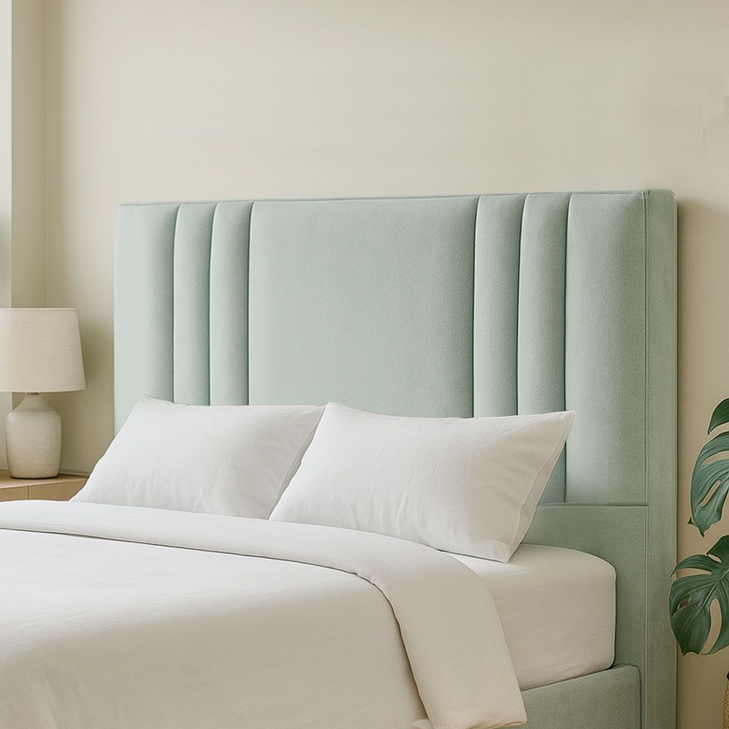 Un cabecero tapizado de color verde menta pálido con capitoné, situado detrás de una cama con ropa de cama blanca, junto a una lámpara de noche.