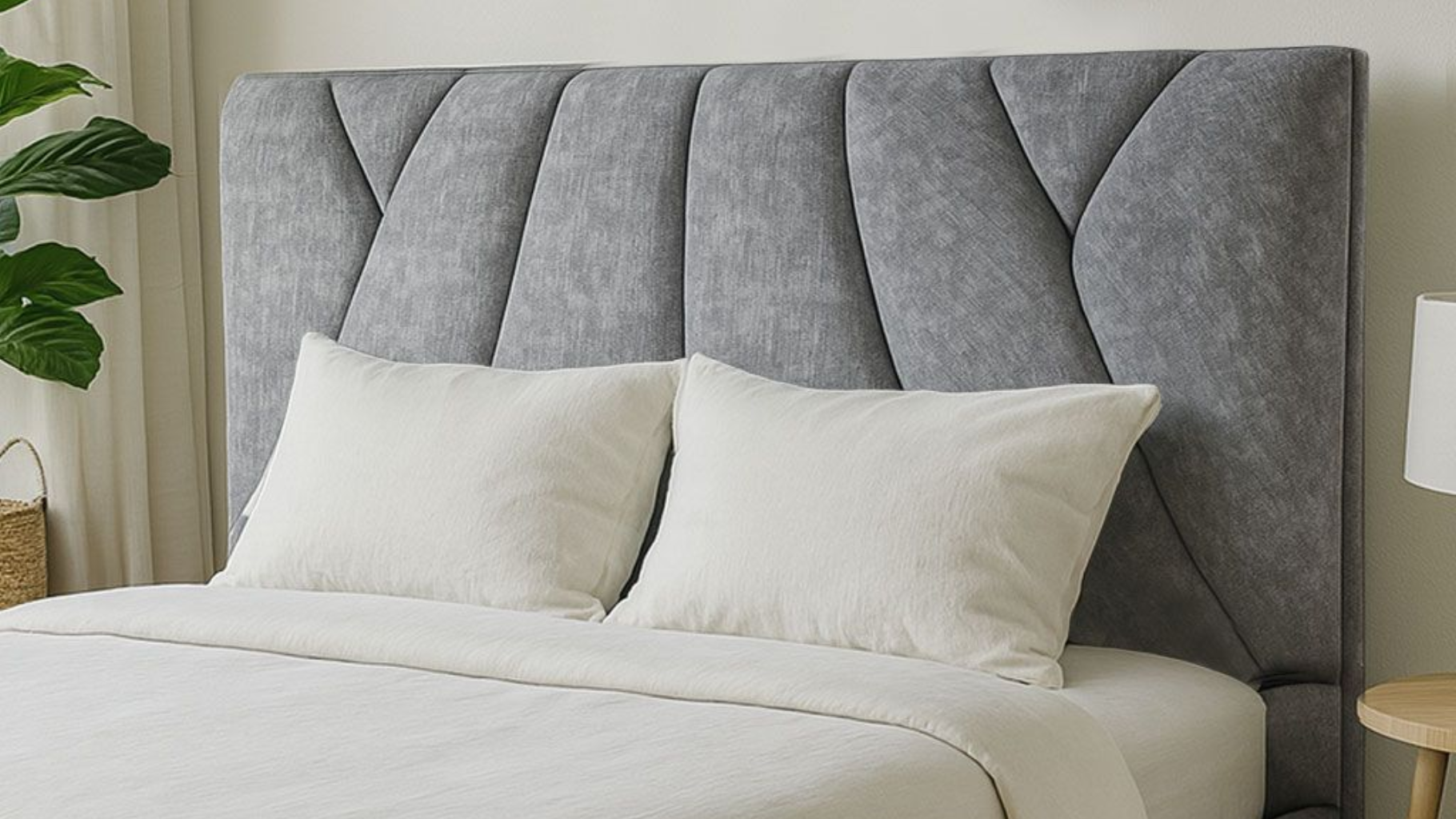 Un cabecero tapizado en gris con costuras verticales en forma de ondas, centrado detrás de dos almohadas blancas sobre una cama.
