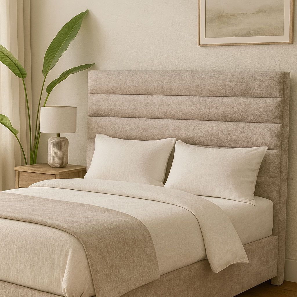 Dormitorio con cabecero tapizado, ropa de cama color crema, mesita de noche con lámpara y una planta.