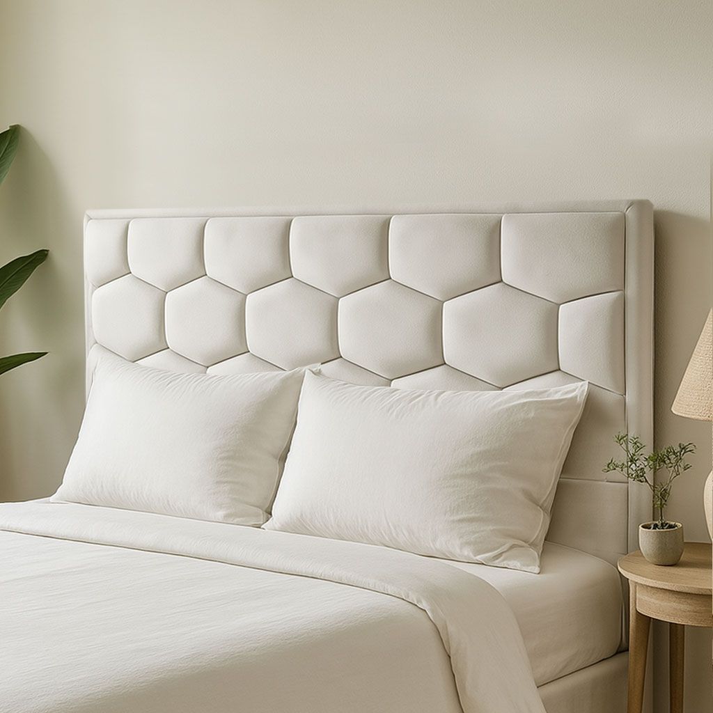 Una escena de dormitorio que muestra un cabecero tapizado de color blanco crema, con capitoné y estampado hexagonal, sobre una cama hecha.