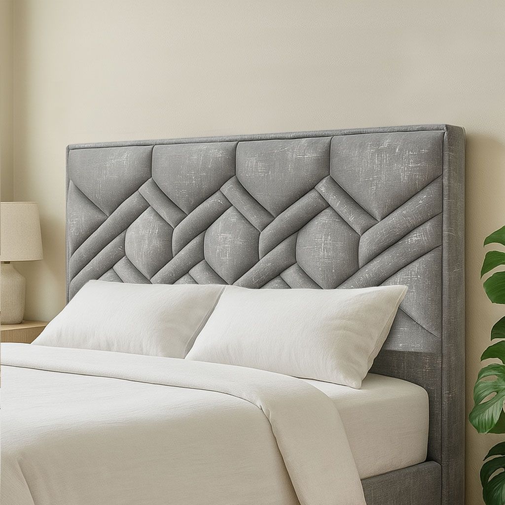Cabecero de cama tapizado en color gris con diseño geométrico, encima de una cama con ropa de cama y almohadas en color blanco.