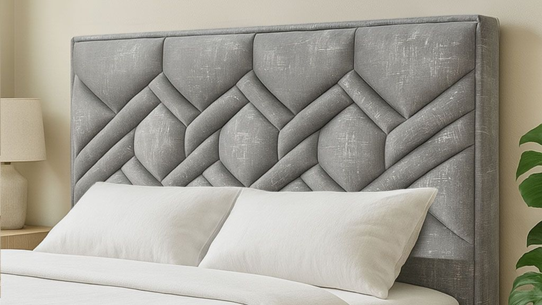 Un cabecero tapizado en gris con un estampado geométrico de rombos acolchados sobre dos almohadas blancas en una cama.