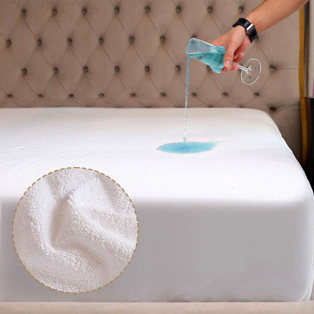 Una mano vierte un líquido azul sobre un protector de colchón blanco, que forma gotas en la superficie junto a una tela en primer plano.