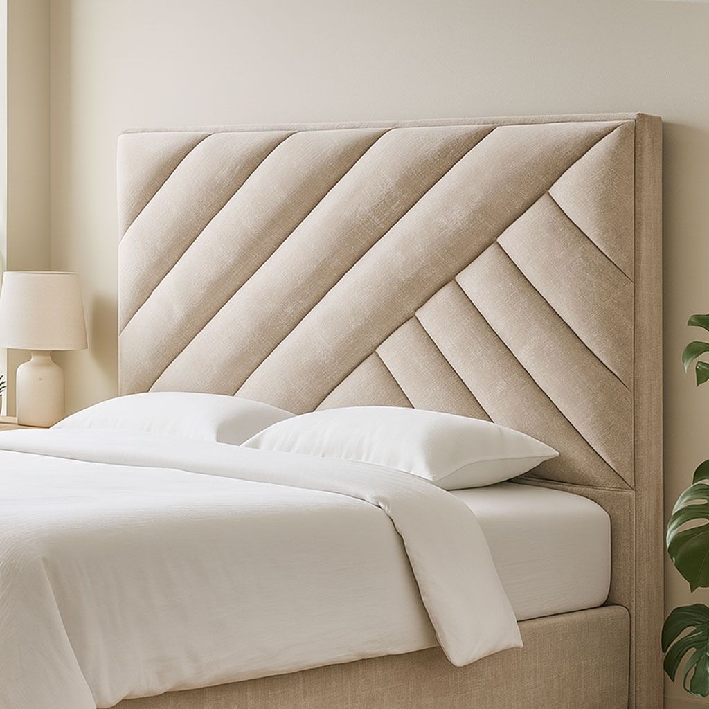 Cabecero de cama tapizado en color beige con paneles en ángulo, en un dormitorio con ropa de cama blanca y lámpara.