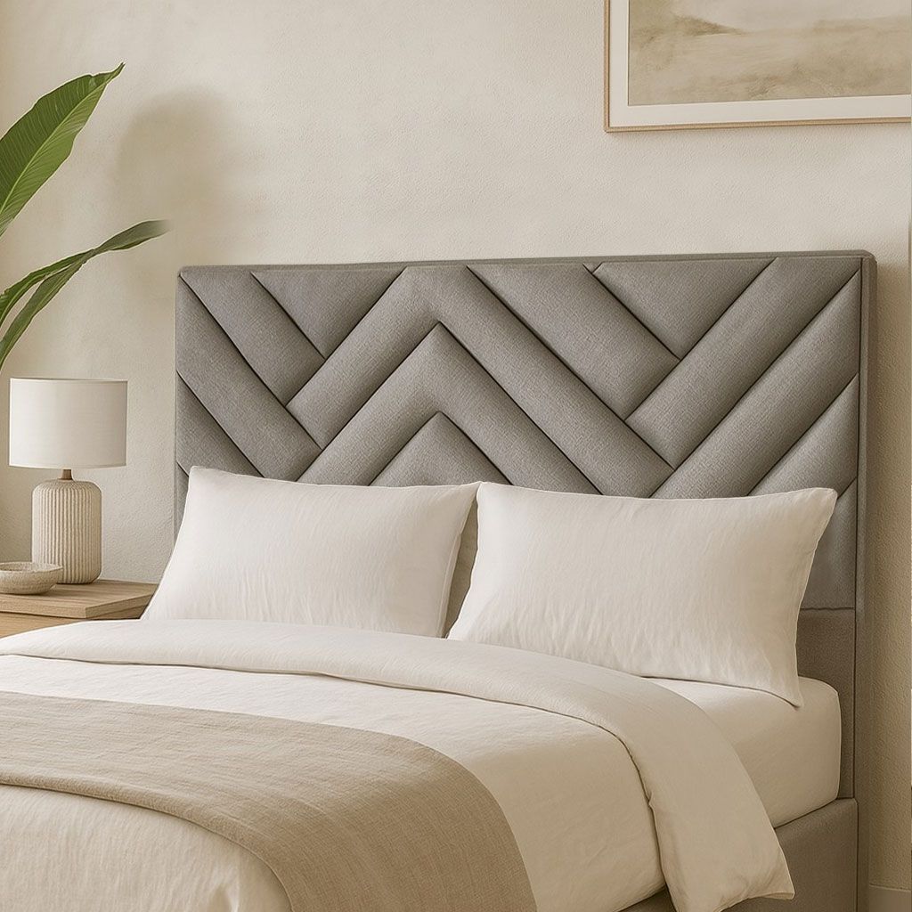 Un cabecero moderno tapizado en gris con un estampado geométrico de espiga, situado detrás de una cama con almohadas blancas.