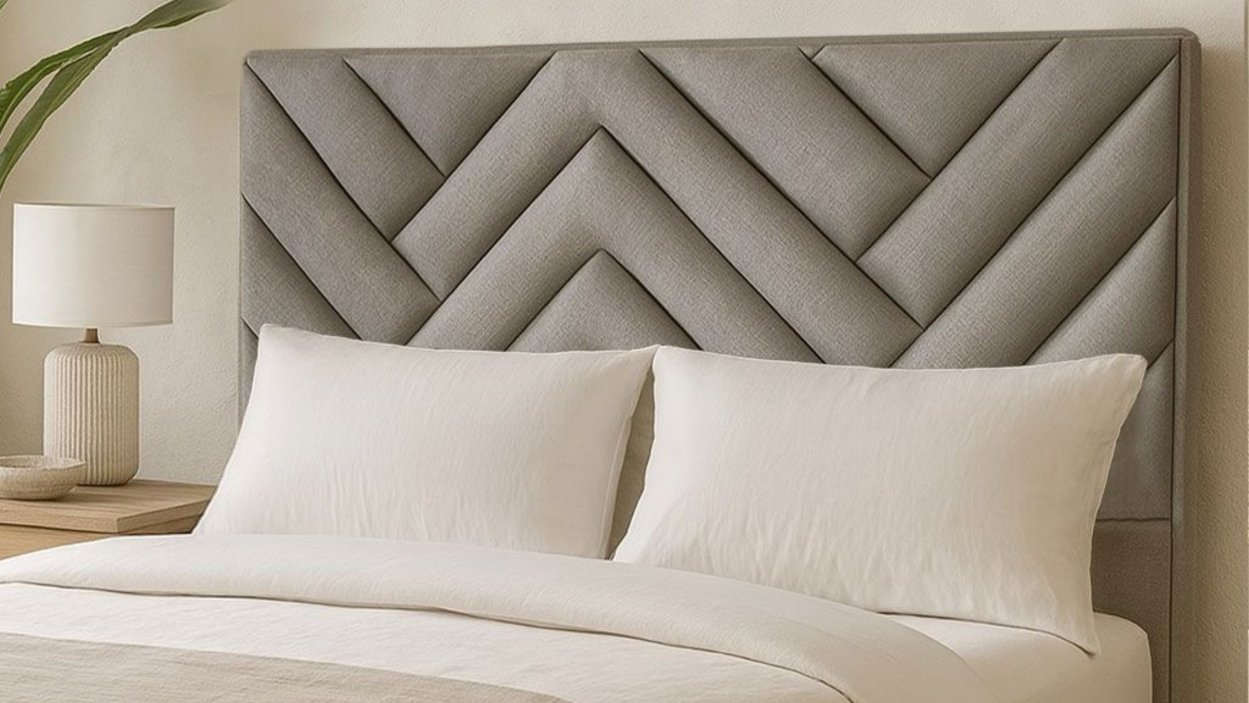 Un cabecero de tela gris con estampado de espiga se sitúa detrás de una cama impecablemente hecha con almohadas blancas y una lámpara de color neutro.