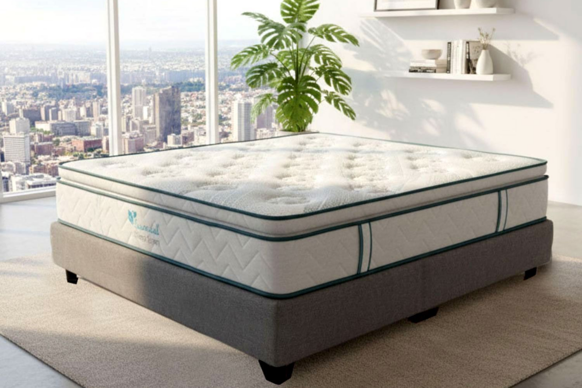 Un colchón con una parte superior blanca y verde azulado sobre una base gris en una habitación con vista a la ciudad.