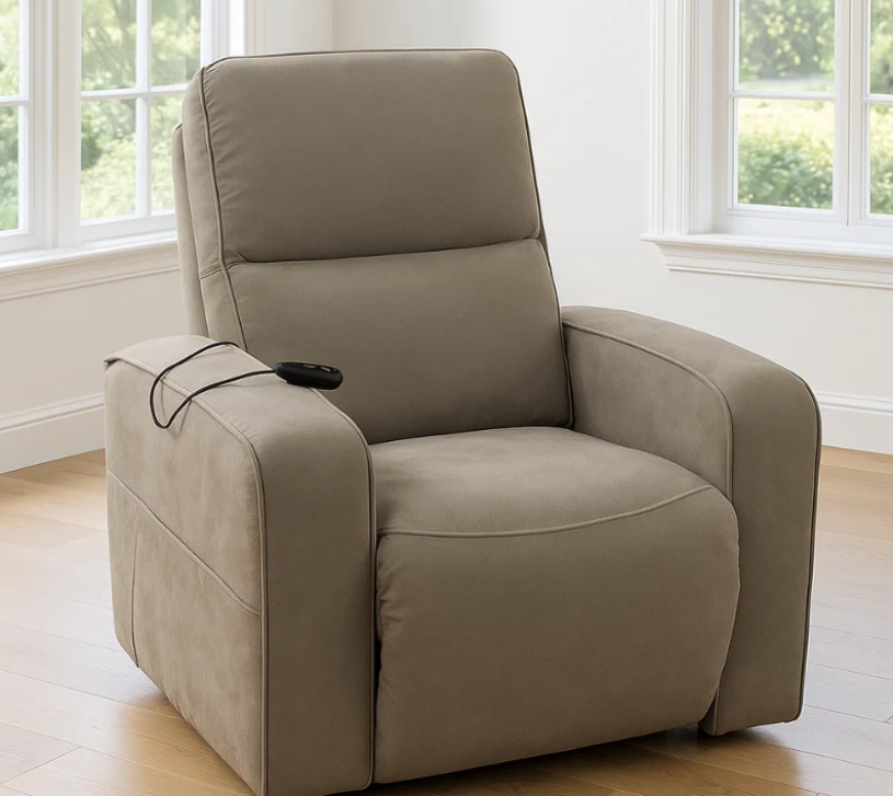 Un sillón reclinable eléctrico de color gris topo con mando a distancia, situado en una habitación luminosa con ventanas.