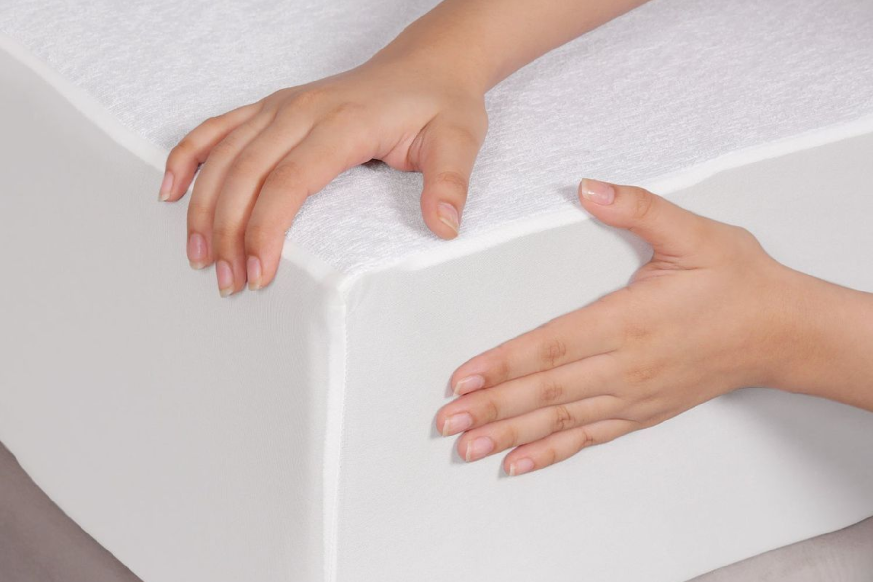 Dos manos tocan la esquina de un protector de colchón blanco extendido sobre un colchón.