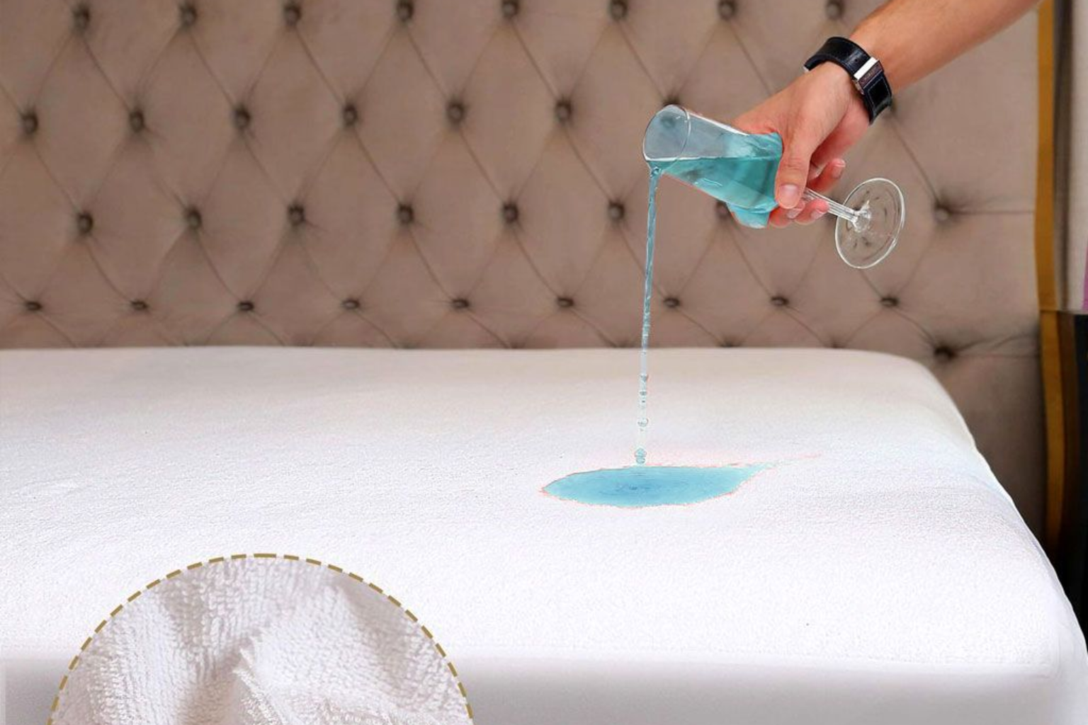 Una persona vierte un líquido azul de un vaso sobre un protector de colchón blanco e impermeable, colocado contra un cabecero acolchado.