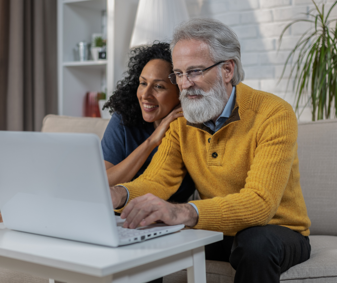 A man and a woman are sitting on a couch using a laptop computer.