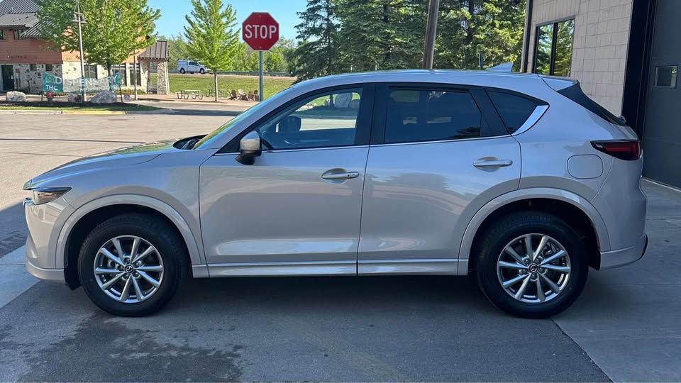 A silver mazda cx-5 is parked in front of a stop sign.