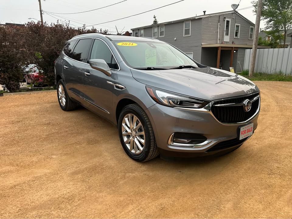 A gray buick enclave is parked in a dirt lot in front of a house.
