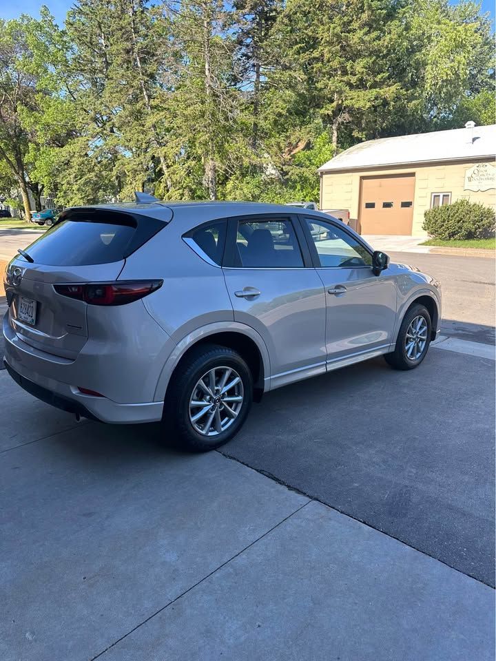 A silver mazda cx-5 is parked in a driveway next to a garage.