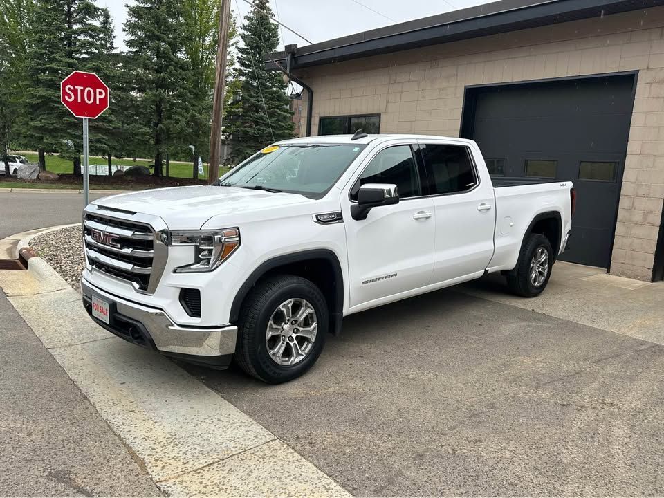 A white pickup truck is parked in front of a garage next to a stop sign.