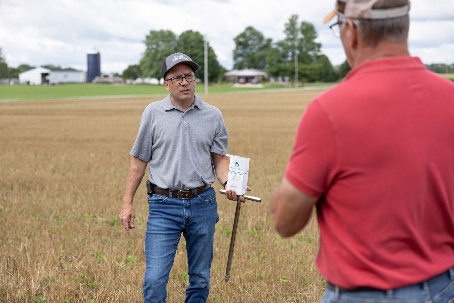 Two men are standing in a field talking to each other.