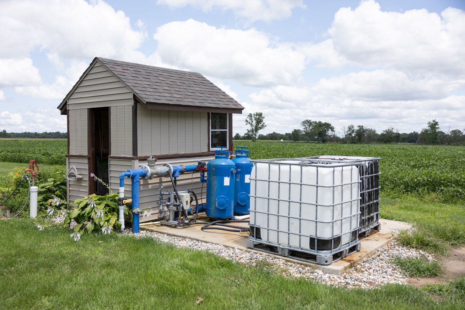 A small irrigation shed is sitting in the middle of a grassy field.