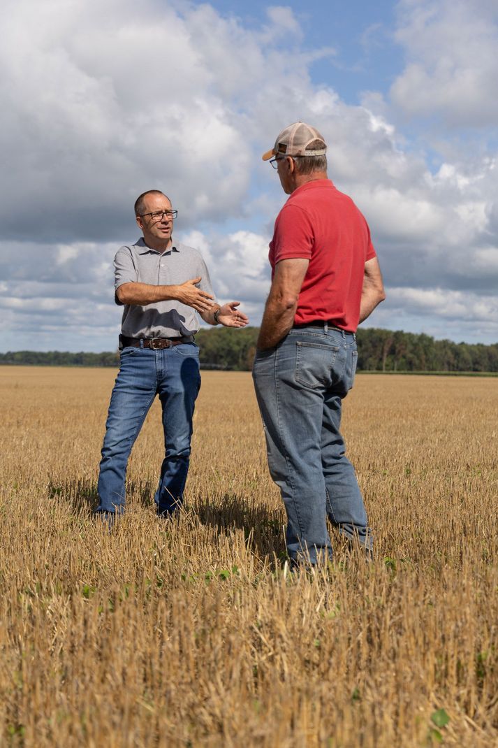 Two men are standing in a field of wheat talking to each other.