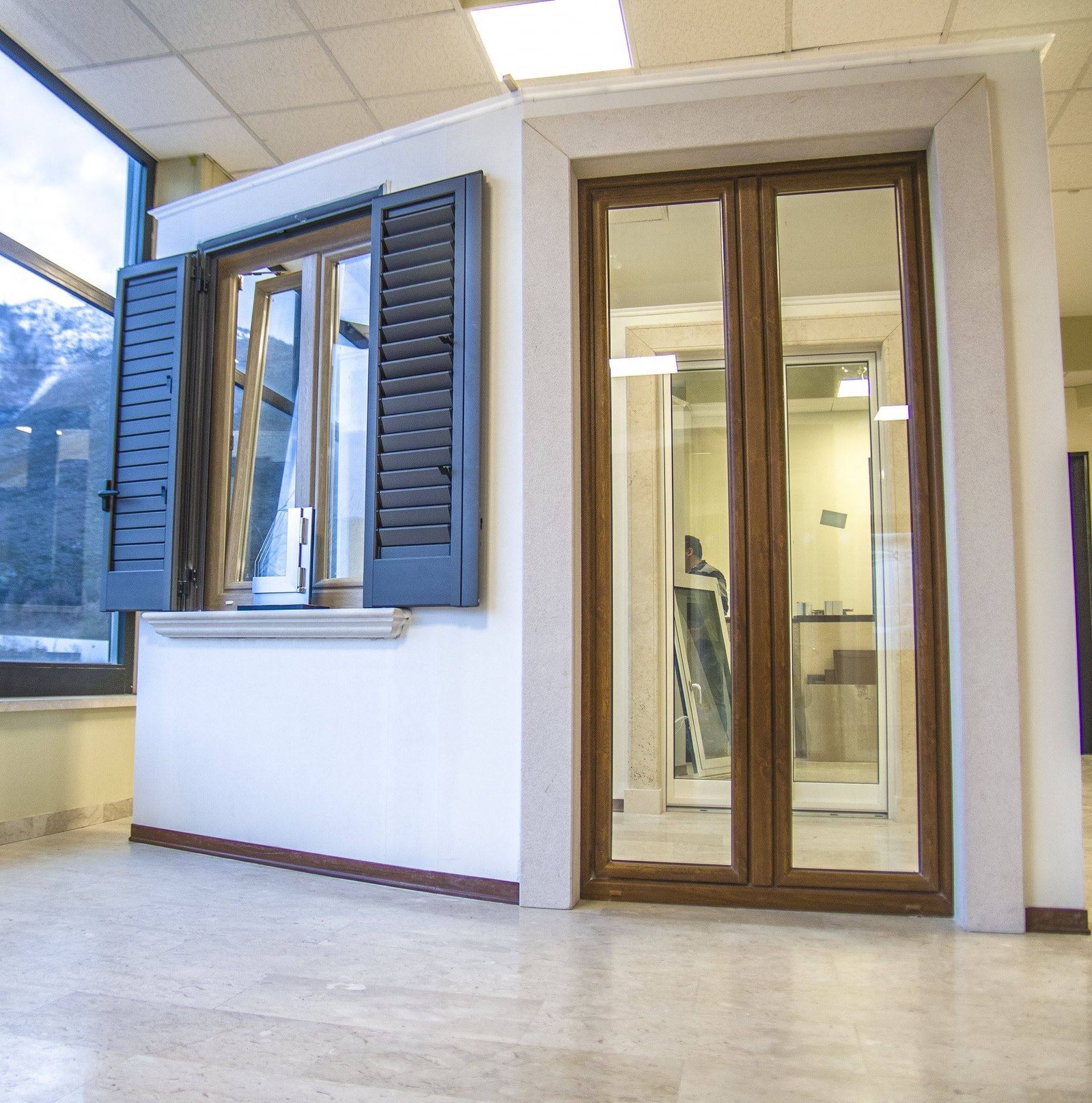 Esposizione di vetrine e porte nello showroom, con cornici in legno, persiane aperte e porte a specchio.