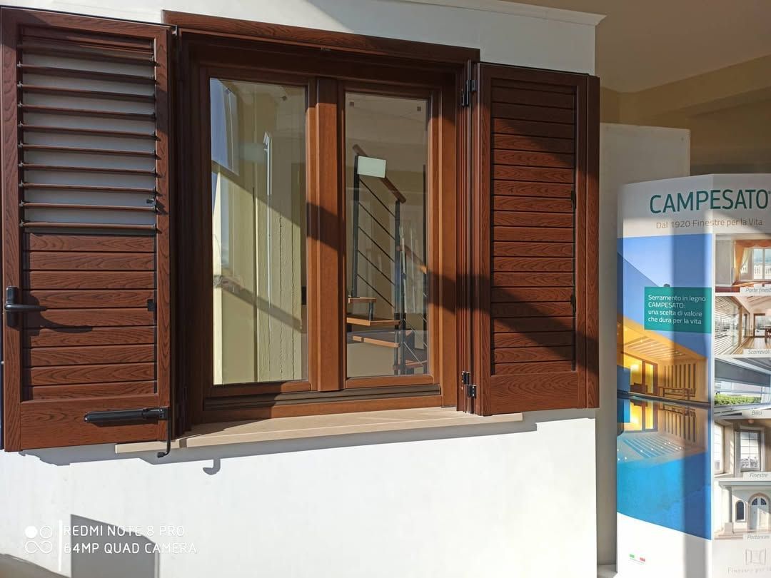 Finestra marrone con persiane aperte su una parete bianca.