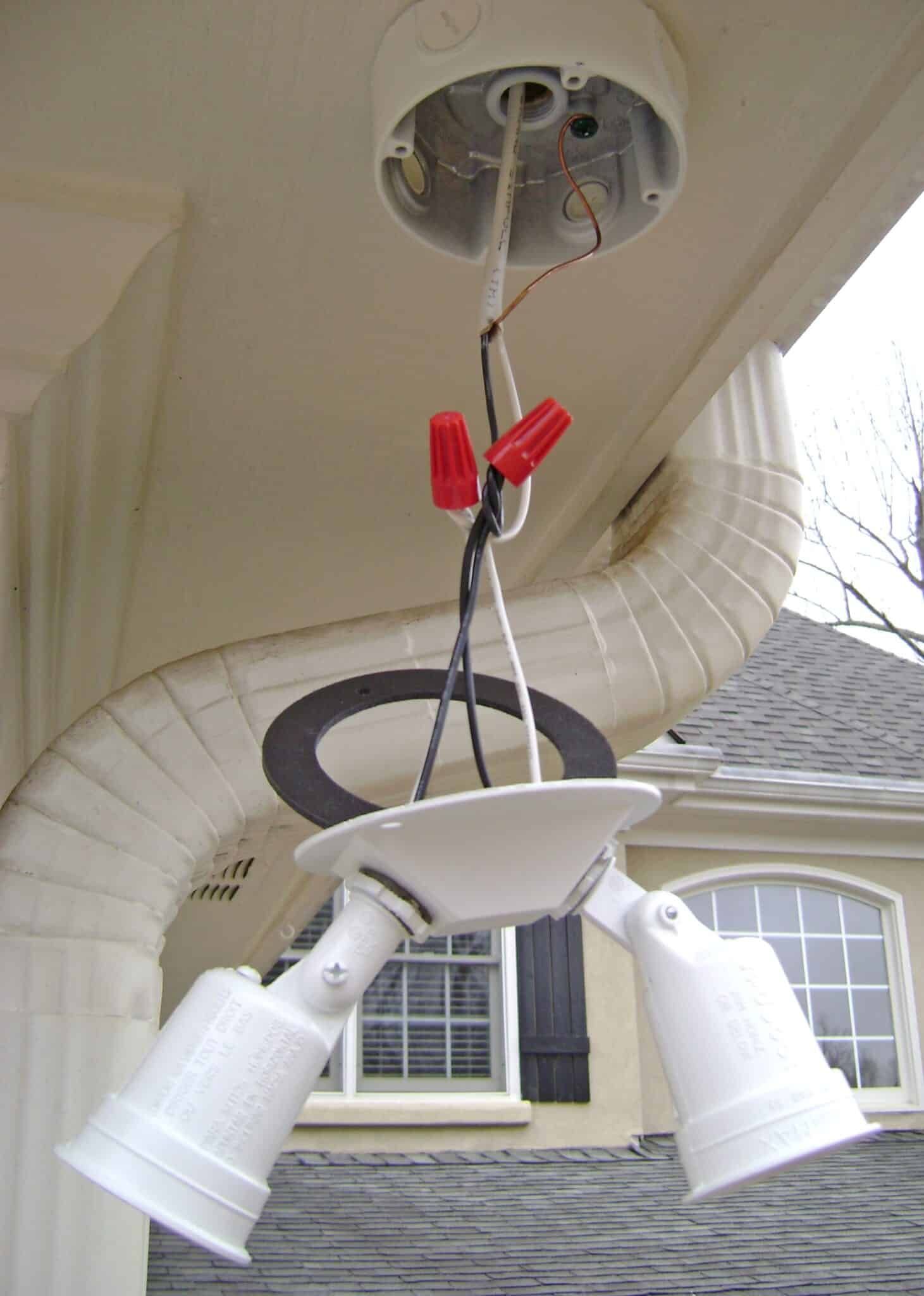 White floodlight fixture hanging from a white electrical box. Wires are exposed, held together with wire connectors.