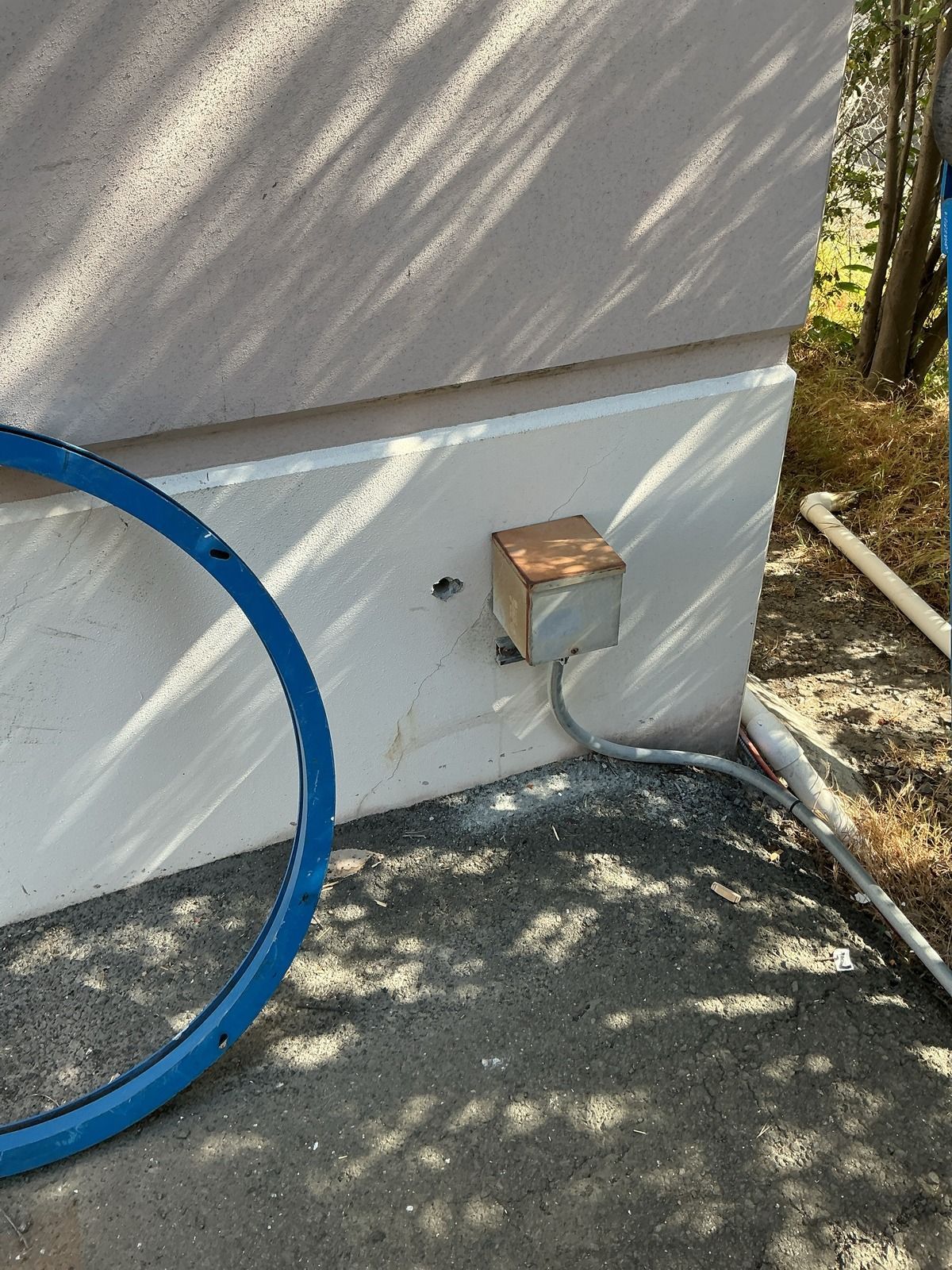 A beige wall with a wooden electrical box and gray conduit cable. A blue ring and a white pipe are nearby.