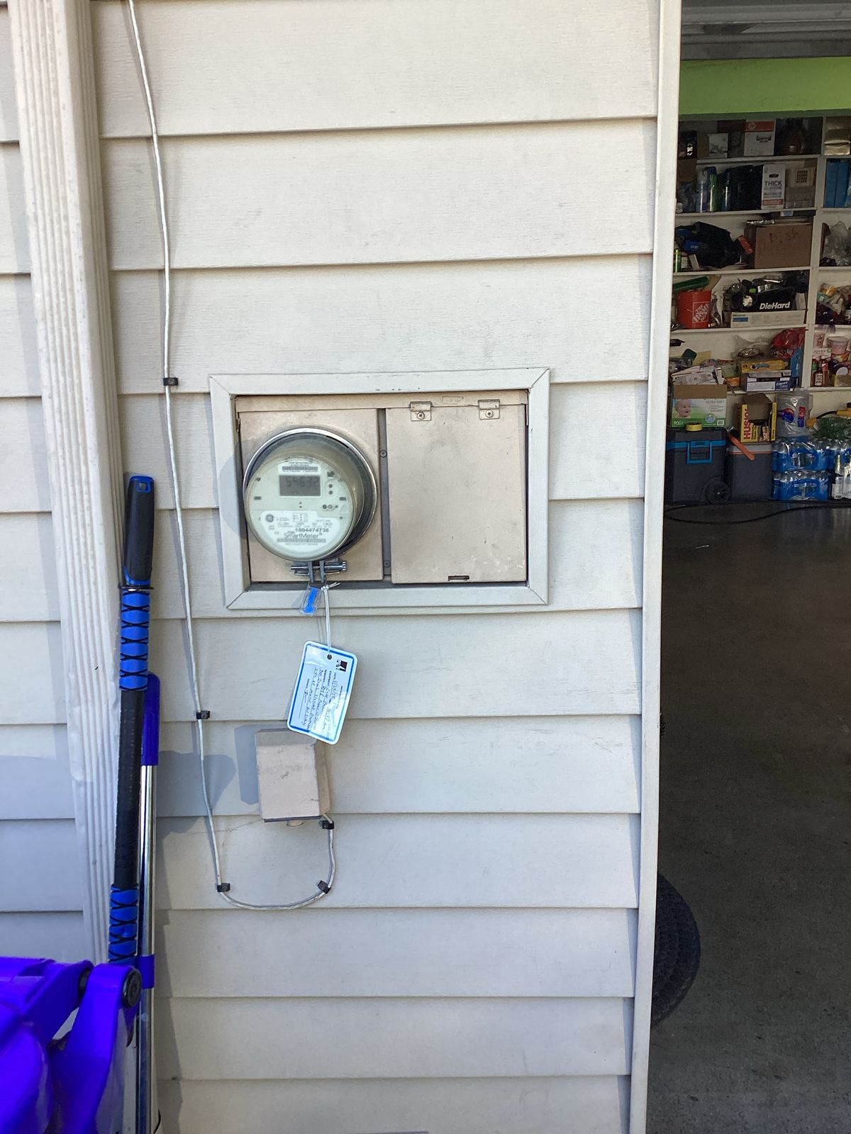 A water meter and blank panel on beige siding, likely a building's exterior.