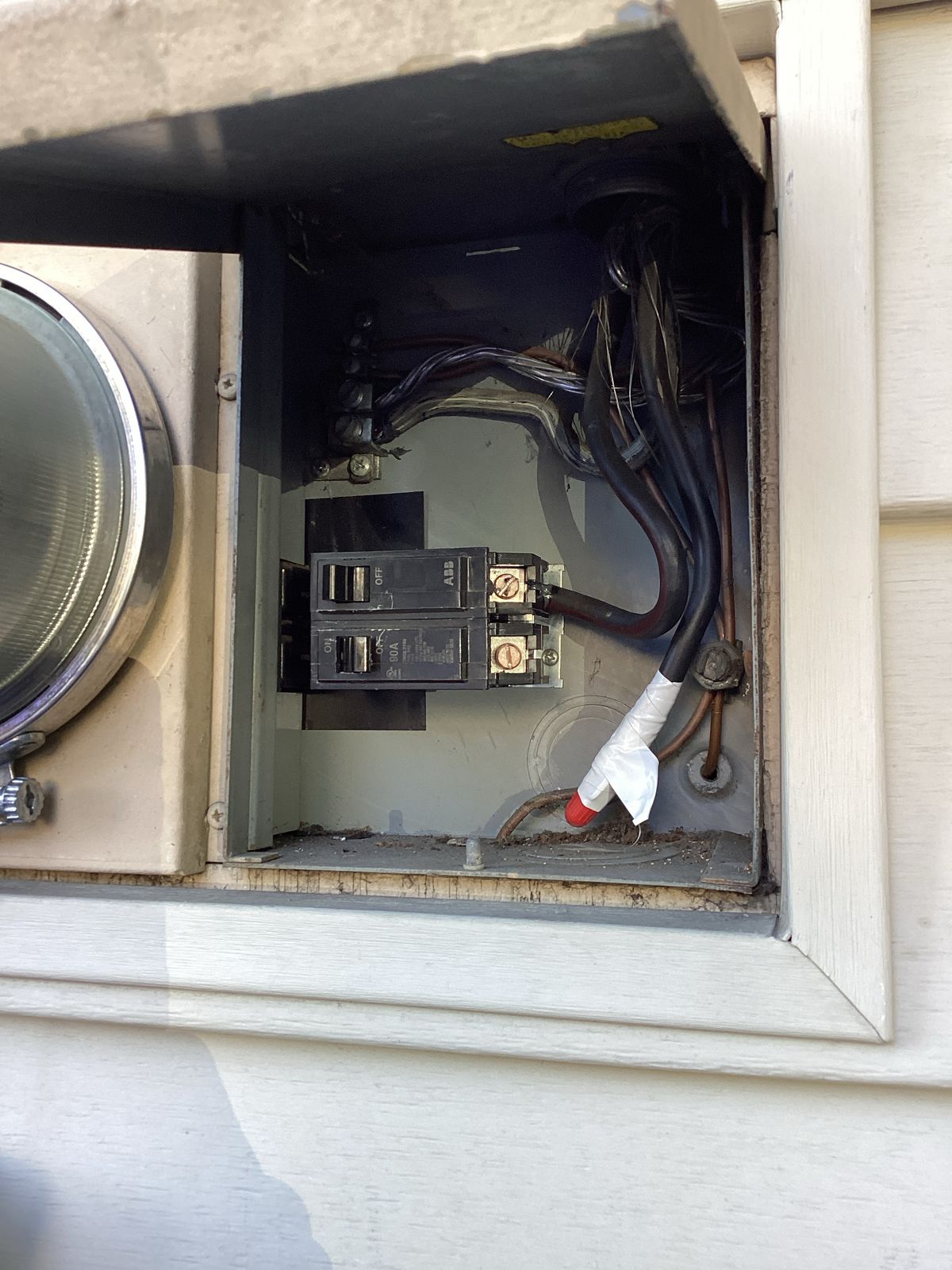Open electrical box with circuit breakers and wiring on a house exterior.