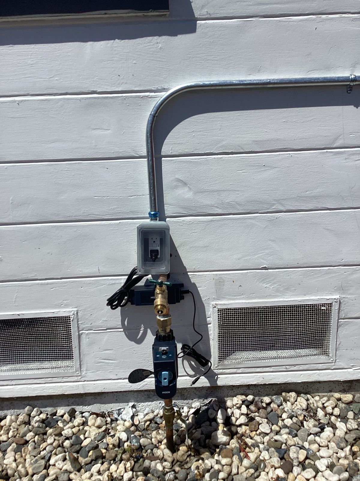 Water valve setup on a white house exterior with electrical conduit and a control box.