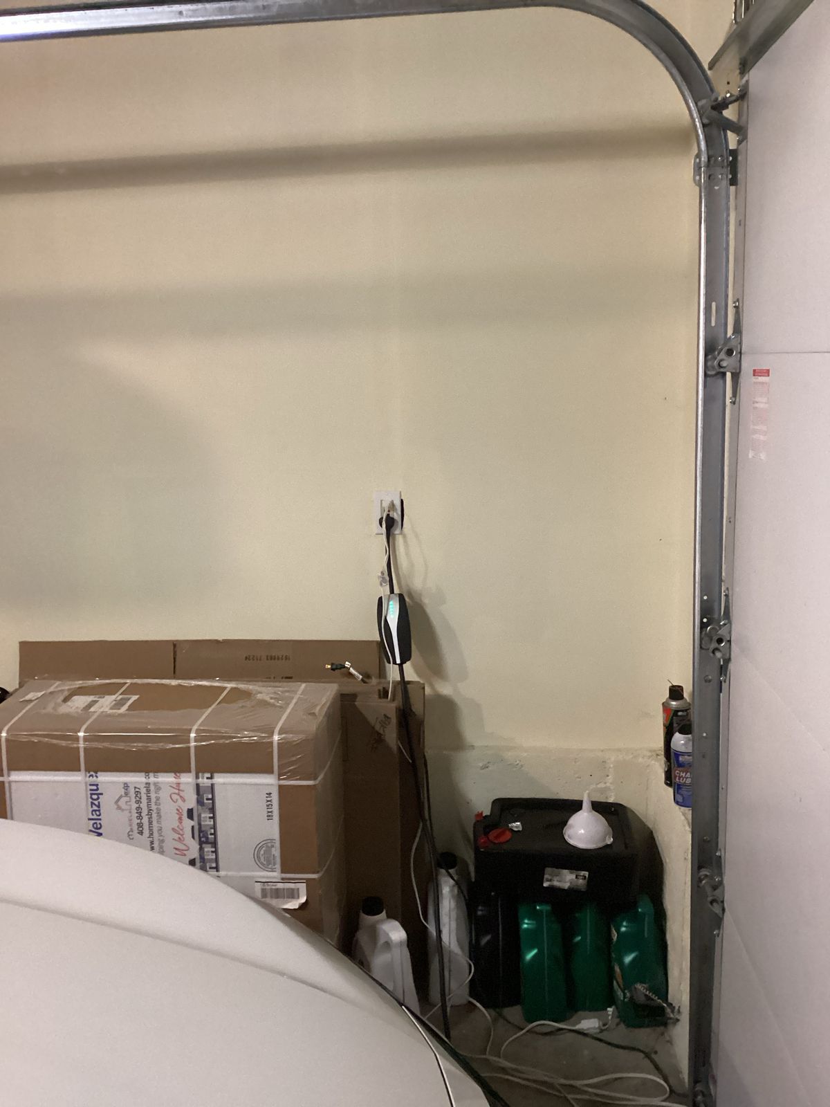 A garage interior with a car, boxes, oil, and a garage door track against a beige wall.