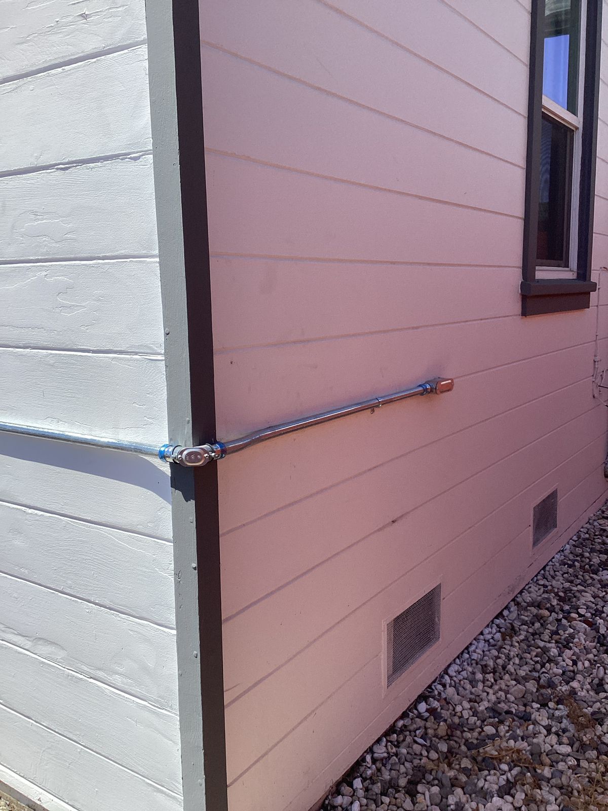 Exterior corner of a building, with gray trim and light pink siding; metal conduit runs horizontally.