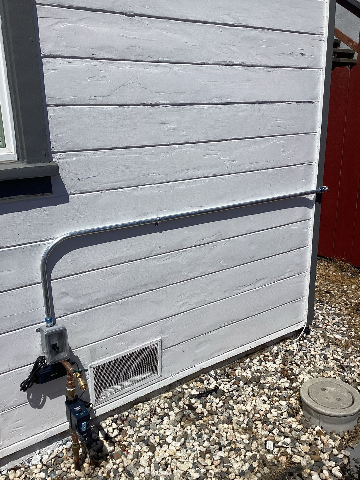 Exterior building wall with electrical conduit and outlet, gravel ground.