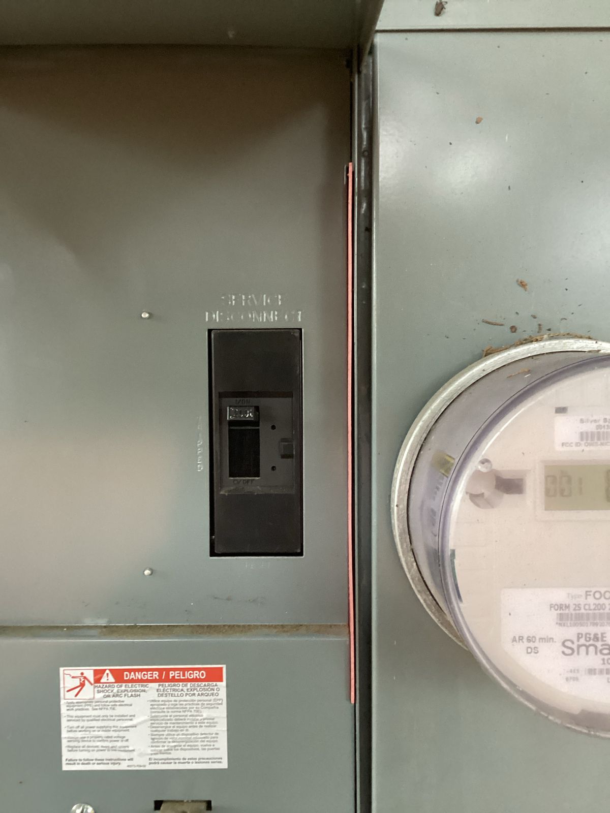 Electrical panel with circuit breaker, meter on the side, and safety warning labels.