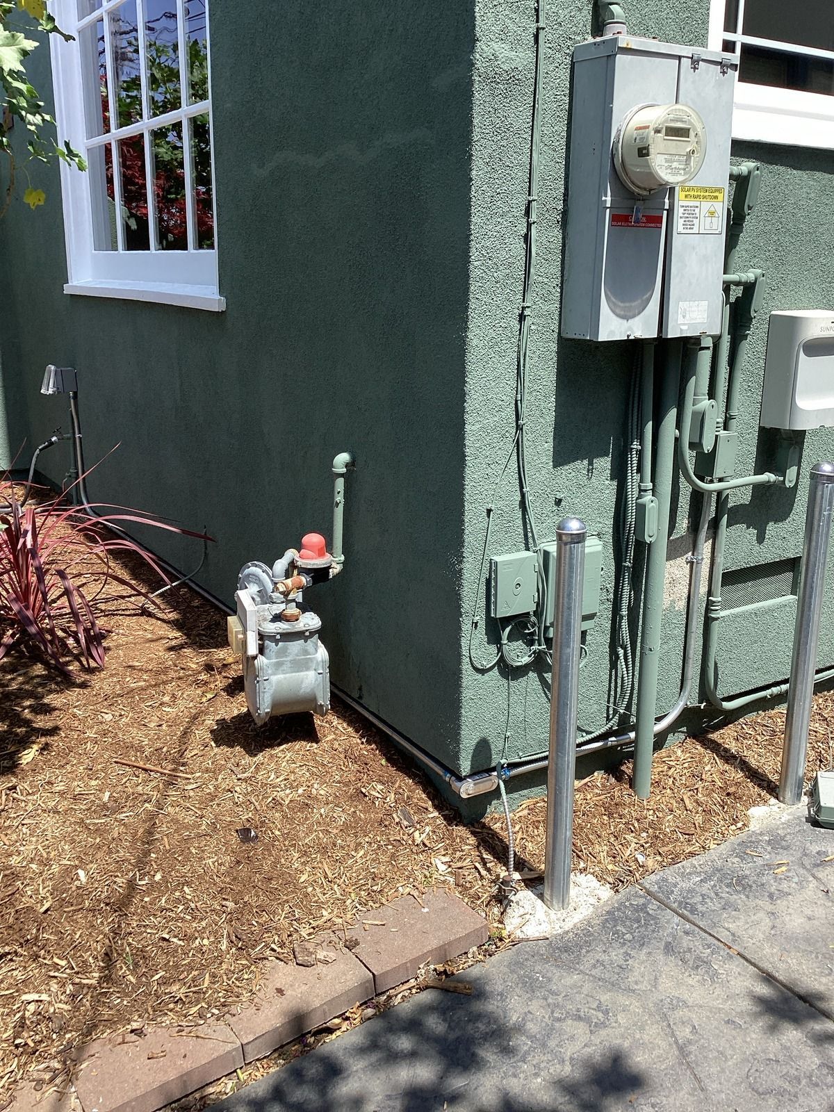 Exterior view of a teal building corner with a gas meter and electrical box.