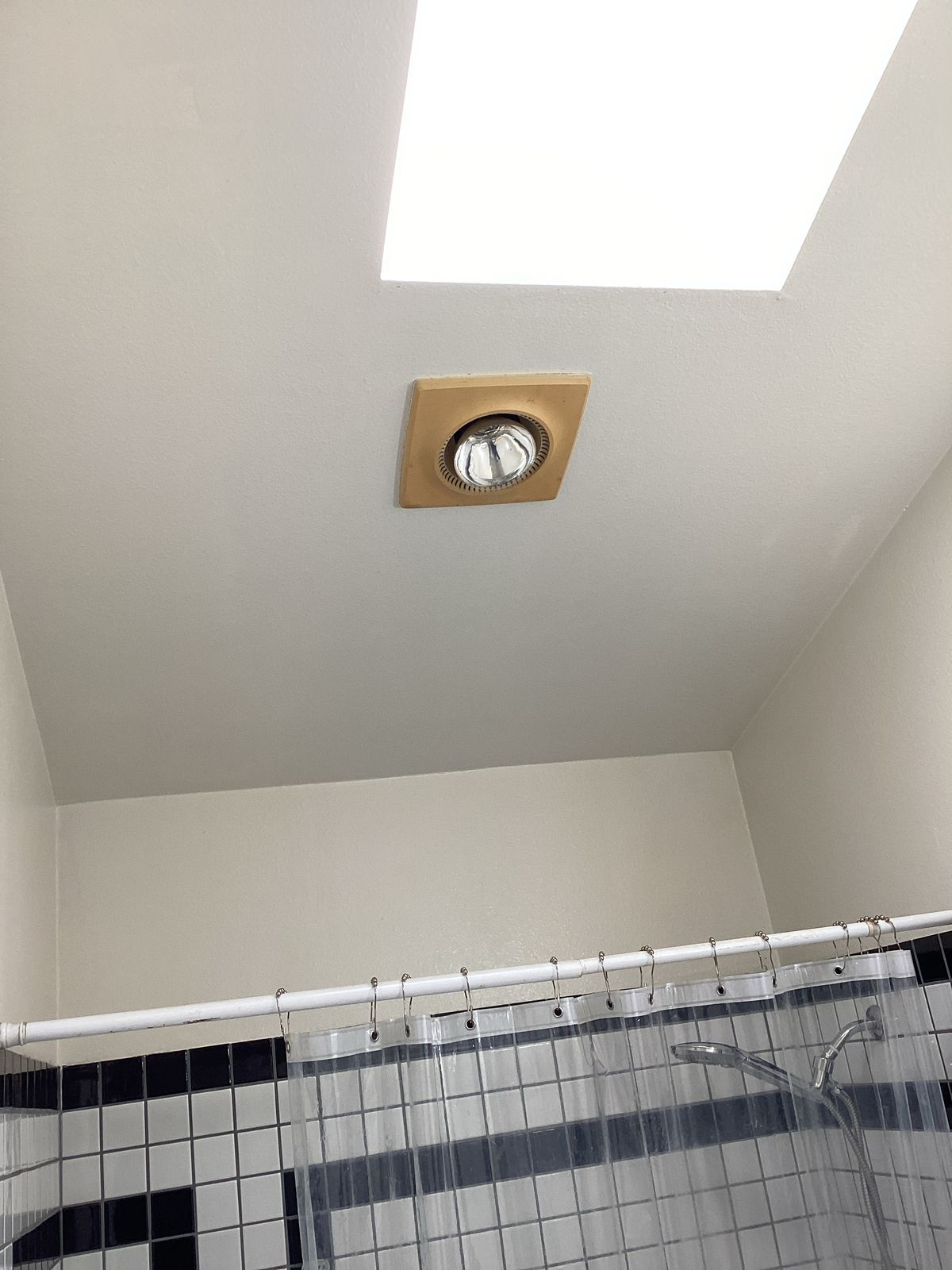 Bathroom ceiling with skylight and light fixture. Shower curtain and tiled wall.