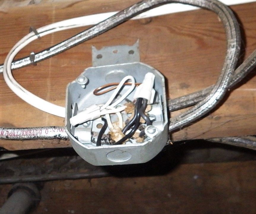 Metal electrical junction box with wires connected inside, mounted on wood.