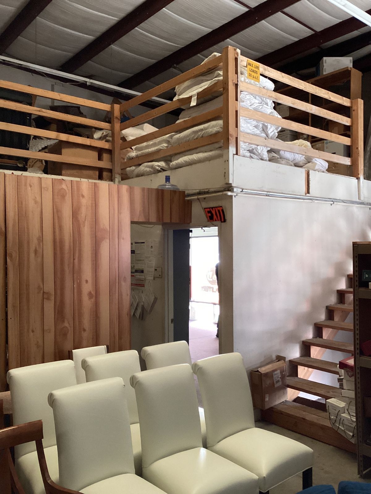 Warehouse interior with white chairs, wood paneling, and a mezzanine with stacked items.