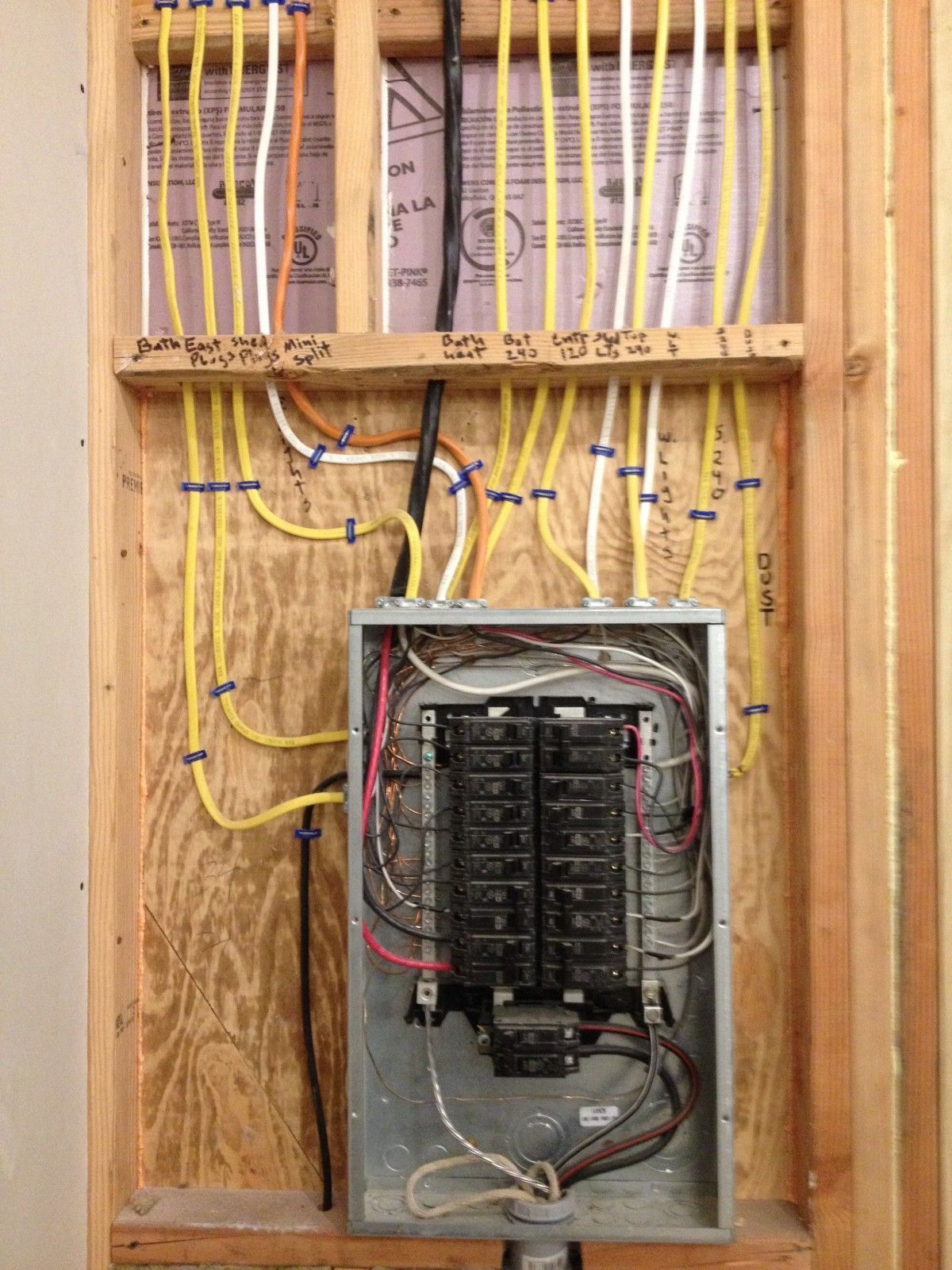Electrical panel installed in a wooden wall. Yellow wires run to the panel, labeled with black text.