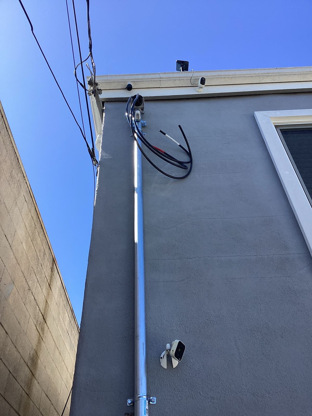 A tall metal pole attached to a building's gray exterior, wires and cables run up the pole.