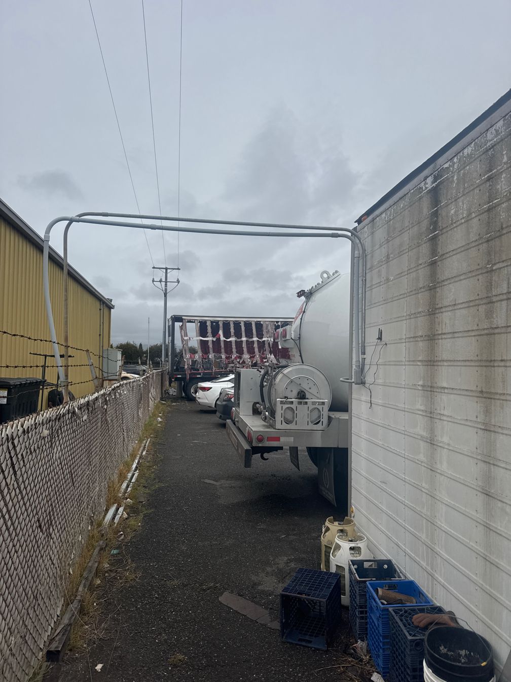 Tanker truck in a narrow alley between buildings, with power lines overhead.